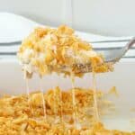 Cheesy ritz cracker chicken casserole on serving spoon. Melted cheese is stretching from the baking dish.