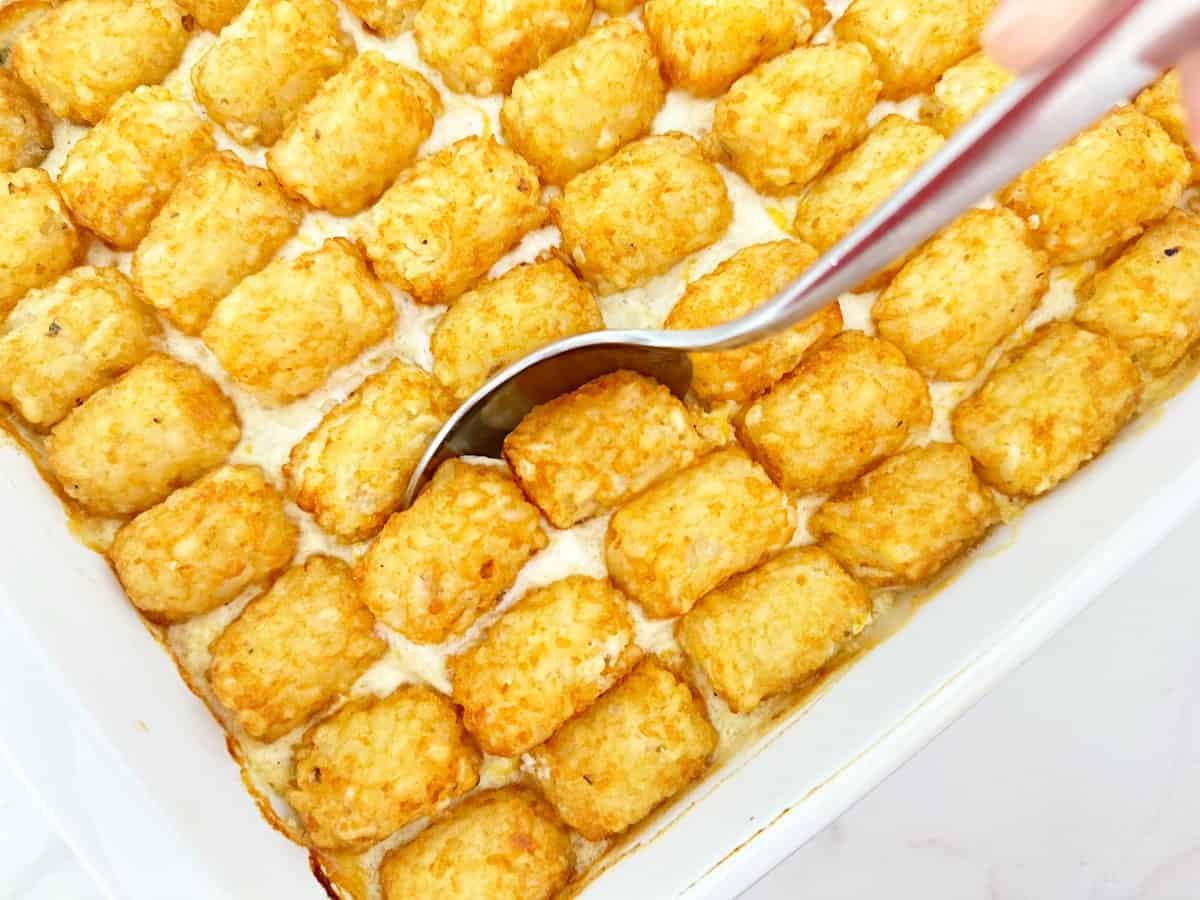 Down view of a silver serving spoon scooping out a portion of tater tot chicken pot pie.