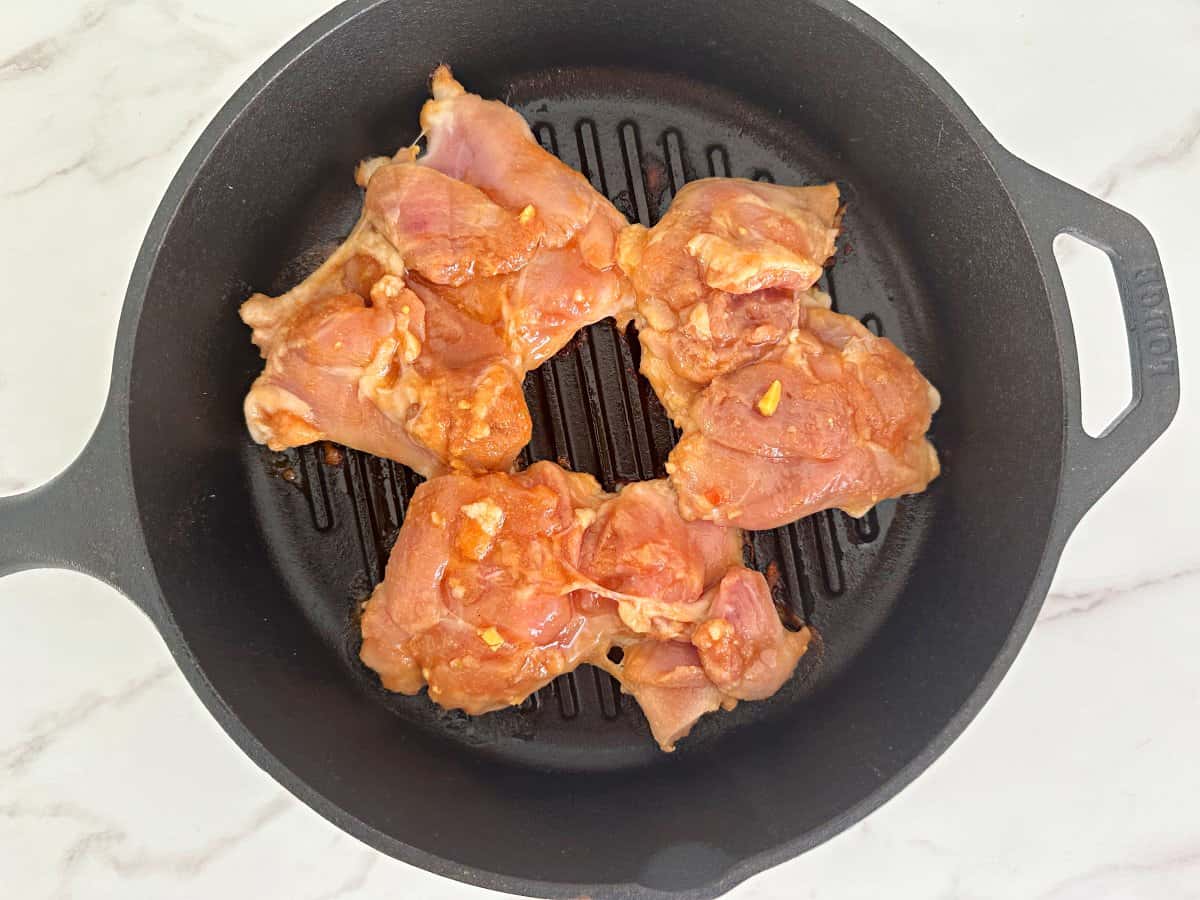 Down view of uncooked chicken thighs in cast iron grill pan.