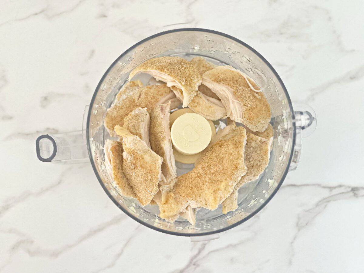 Down view of large chunks of chicken breasts in food processor.