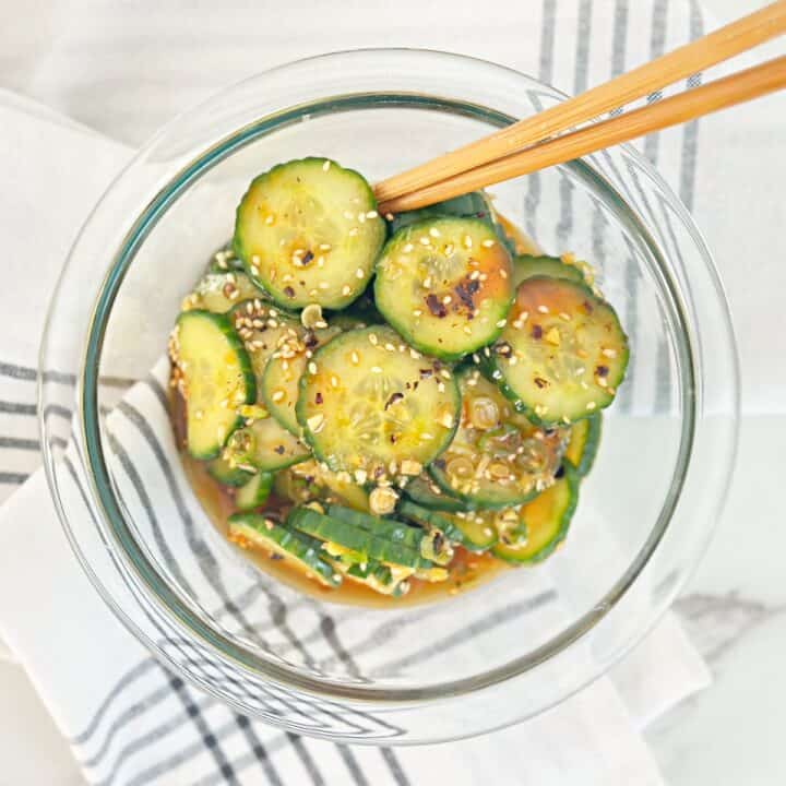 Down view of clear mixing bowl with asian cucumber salad and chopstick.
