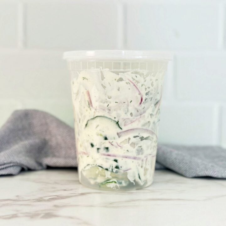 Side view of creamy cucumber salad in deli container.