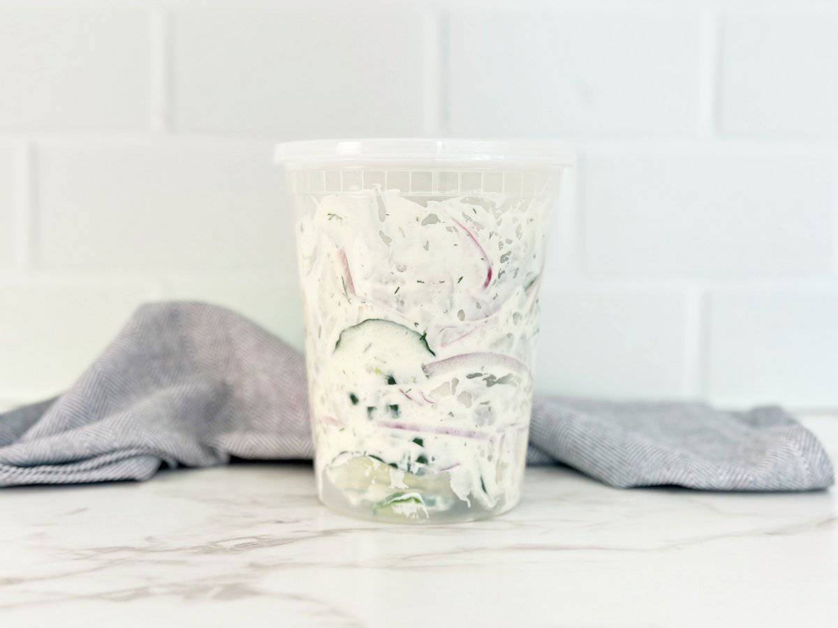 Side view of creamy cucumber salad in deli container.