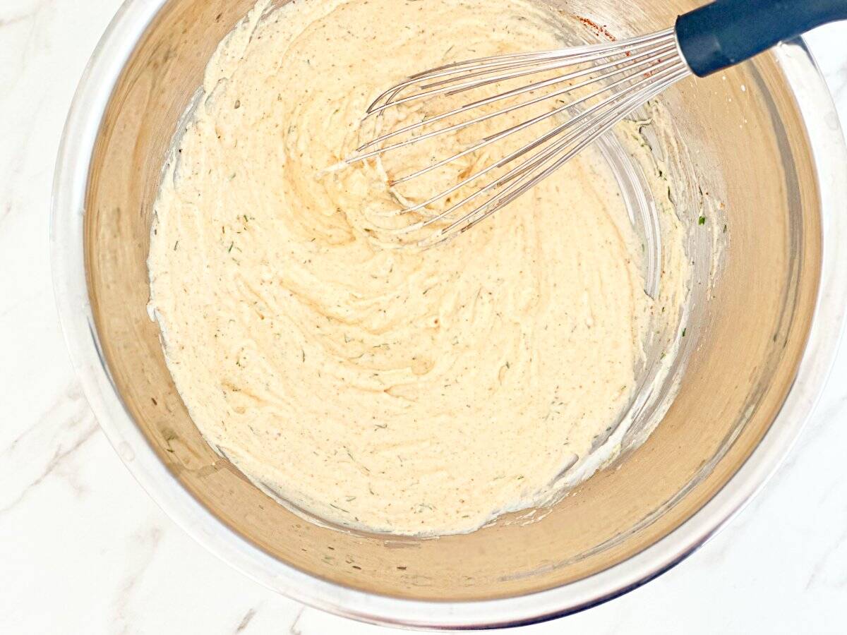 Down view of silver mixing bowl of creamy seafood dressing with whisk.