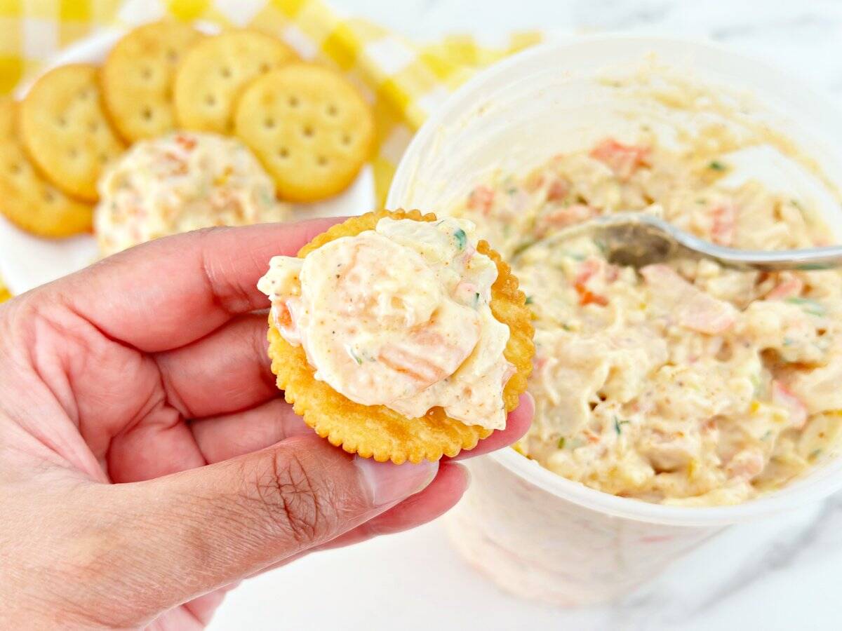 Hand holding seafood salad on a cracker.