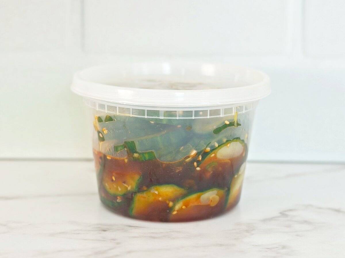 Side view of asian cucumber salad small in deli container.