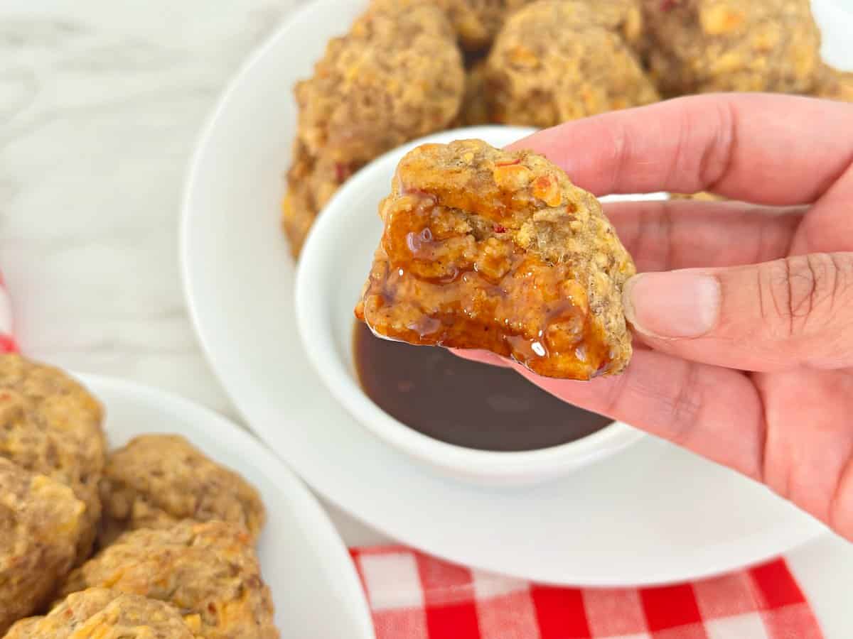 Hand holding a bitten pimento cheese ball dipped in chili sauce.