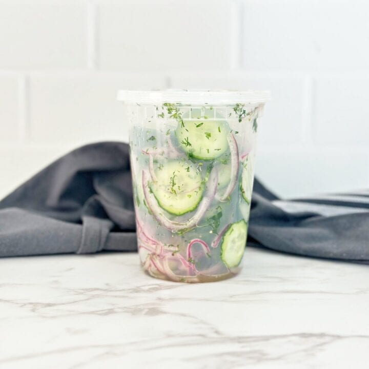 Side view of vinegar cucumber salad with fresh dill in deli container.