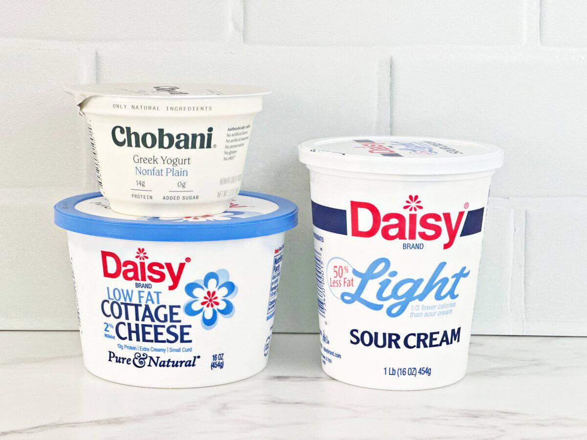 Side view of plain greek yogurt, light sour cream, and low fat cottage cheese in their plastic packaging.