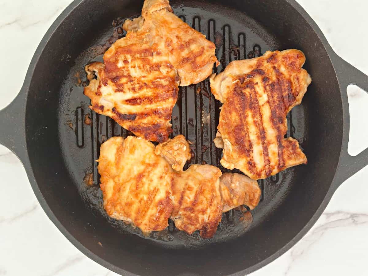 Down view of cooked chicken thighs with grill marks in cast iron grill pan.