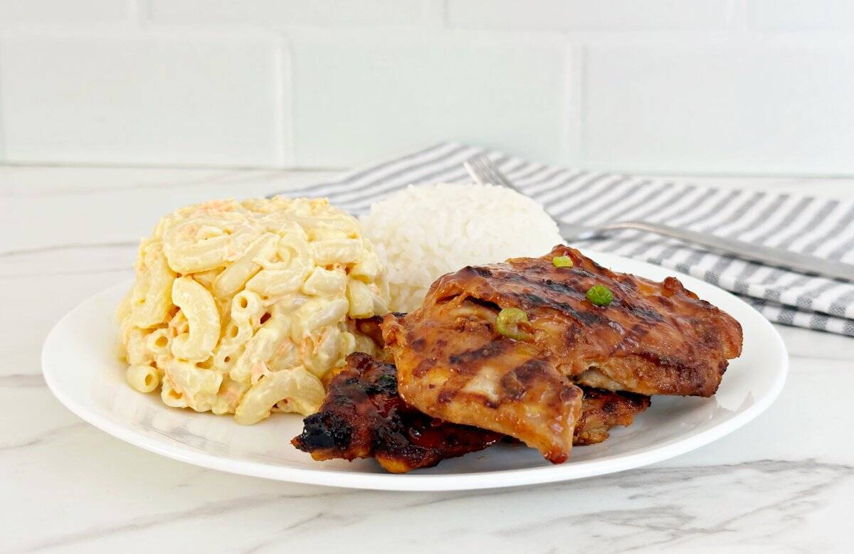 Side view of huli huli Hawaiian chicken bbq plate. Side of Macaroni salad, white rice, and grilled chicken thighs.