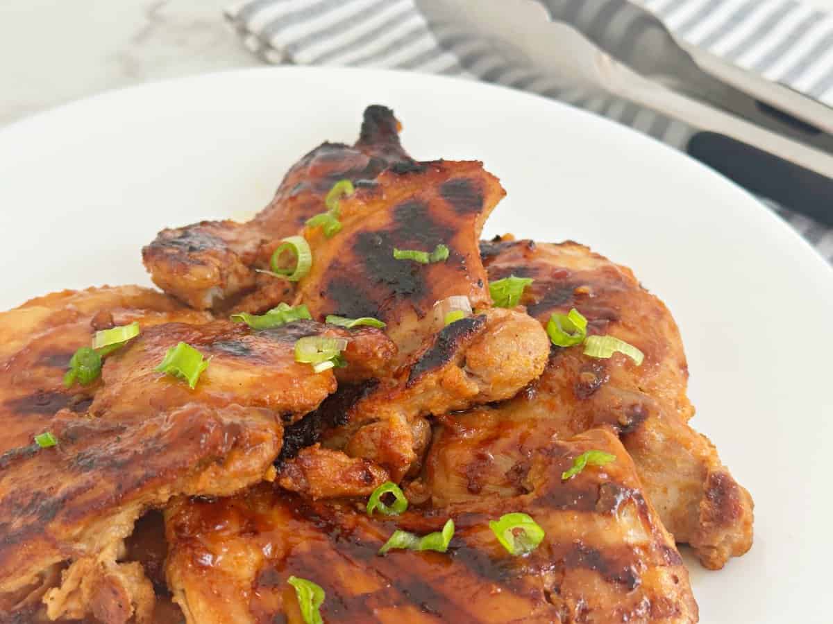 Side view of huli huli Hawaiian chicken thighs on white plate.