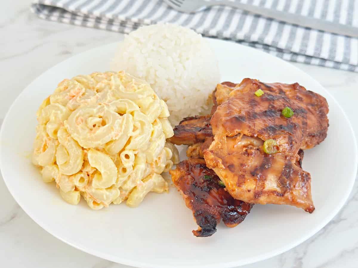 Side view of huli huli Hawaiian chicken bbq plate. Side of Macaroni salad, white rice, and grilled chicken thighs.