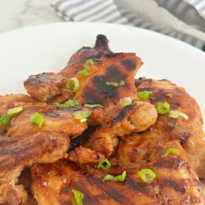 Side view of huli huli Hawaiian chicken thighs on white plate.