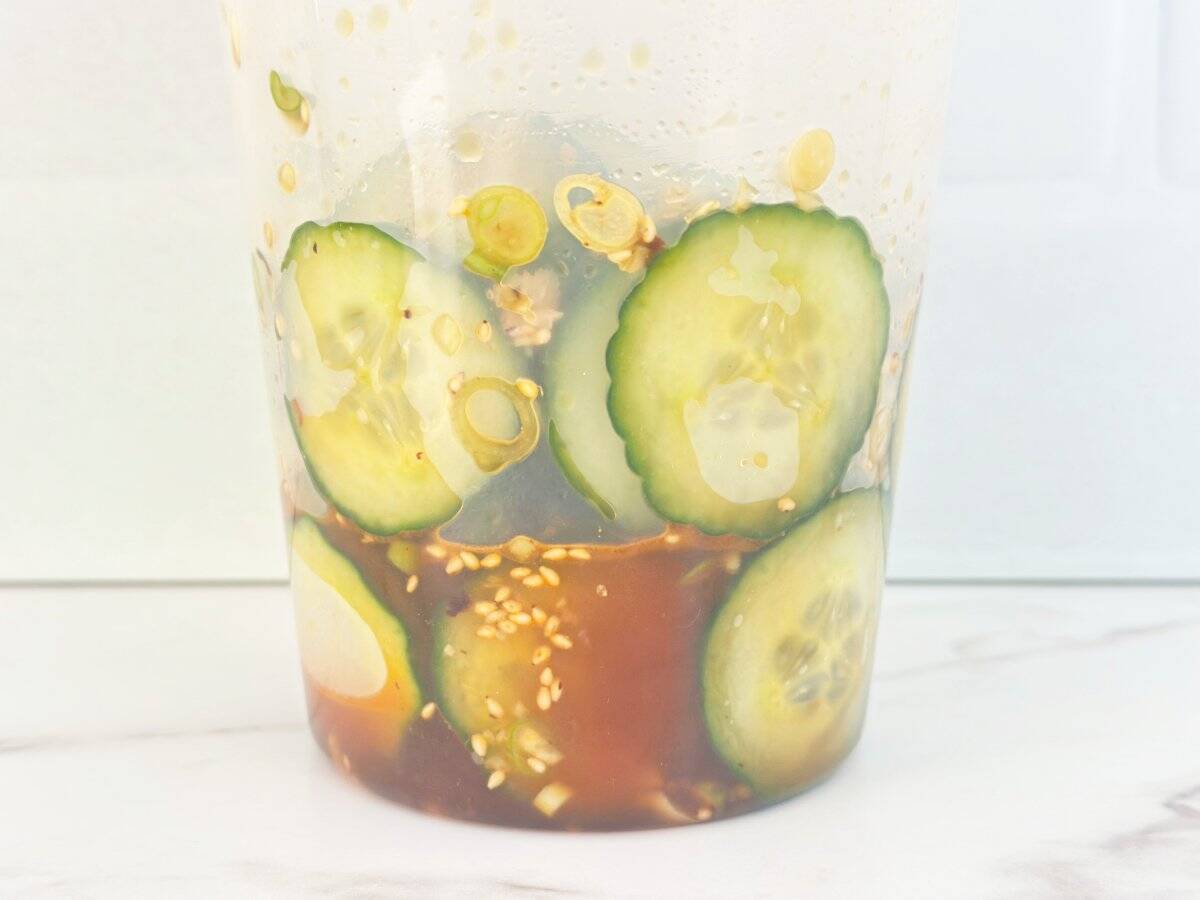 Down view of shaken asian cumber salad in a deli container.