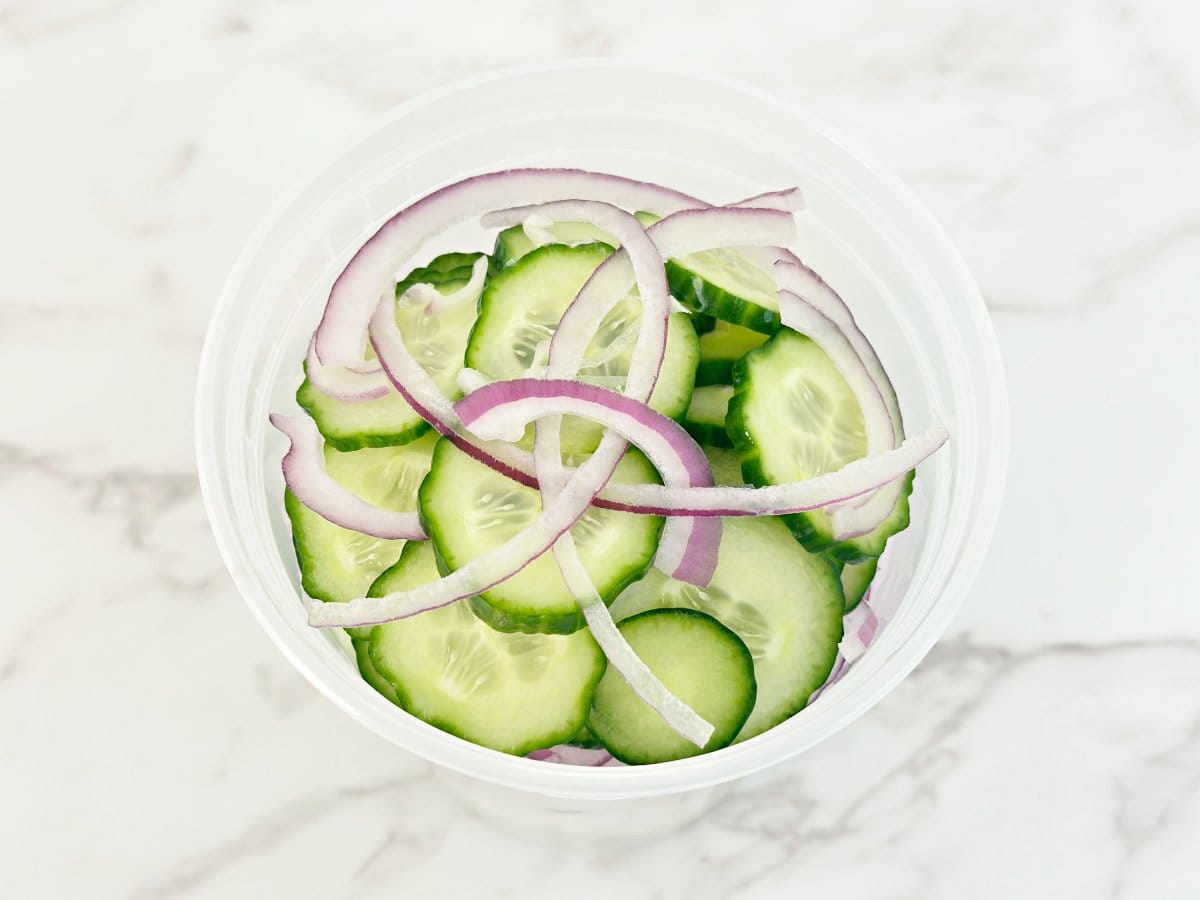 Down view of deli container with sliced cucumbers and onions.