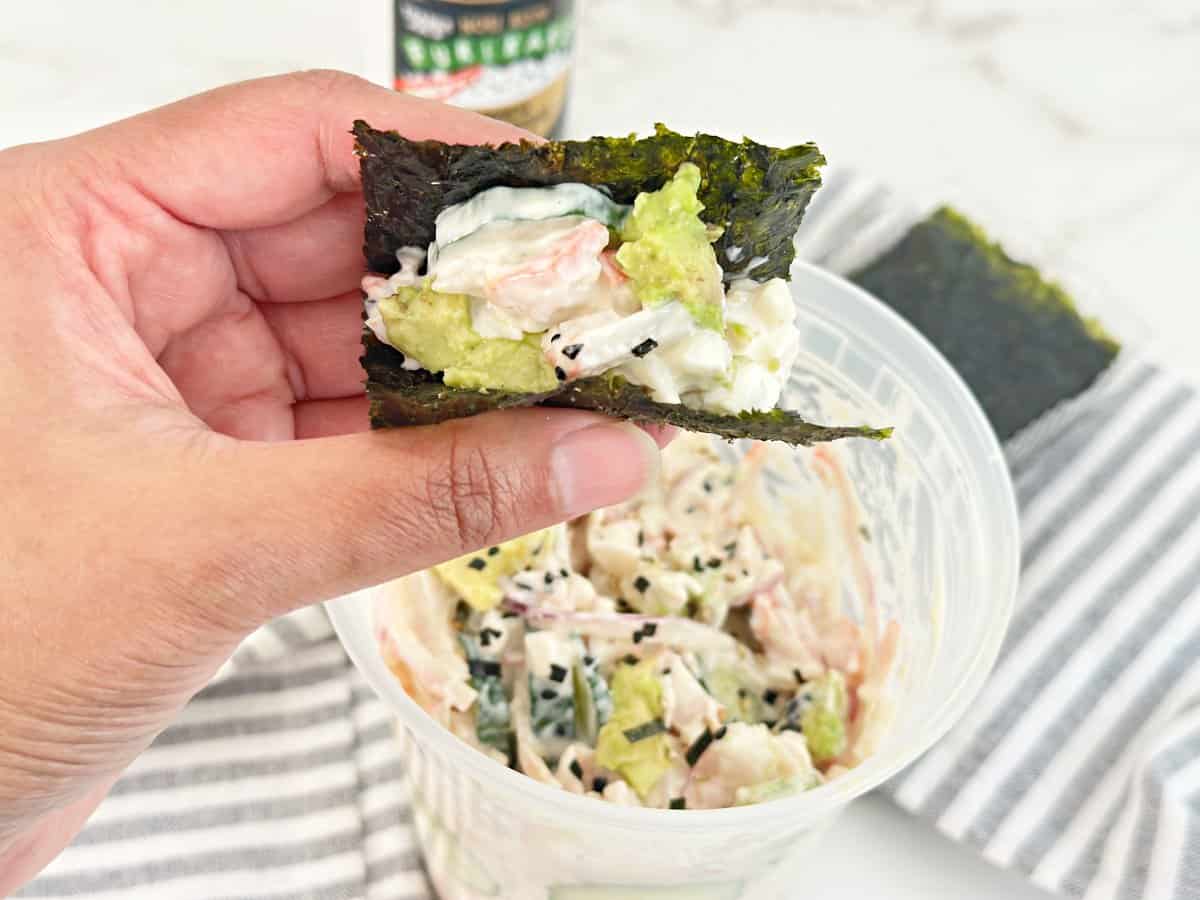 Hand holding roasted seaweed sheet wrapped with sushi cucumber salad.