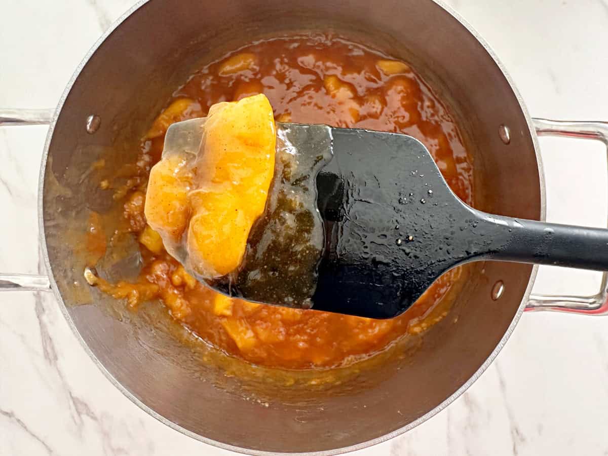 Black rubber spatula with cooked spiced peaches.