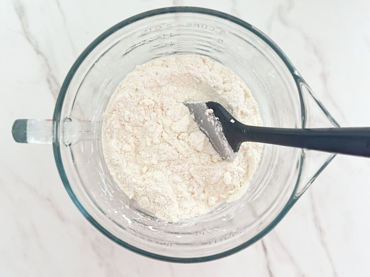 Down view of dry biscuit mixture in clear mixing bowl.