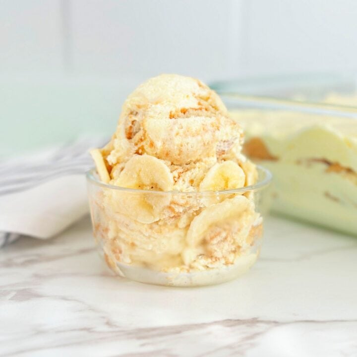 Scoop of fluffy banana pudding with slices of fresh banana in glass container.
