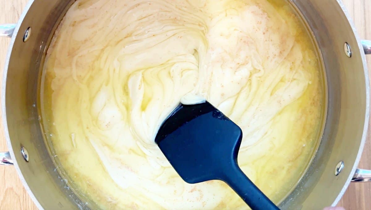 Down view of pot with browned butter and condensed milk. Black rubber spatula mixing.