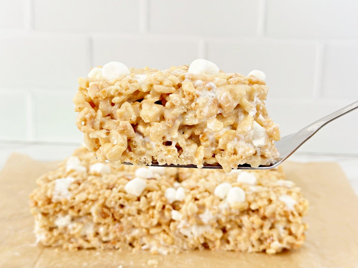 Silver spatula holding a piece of rice krispies treats with condensed milk.