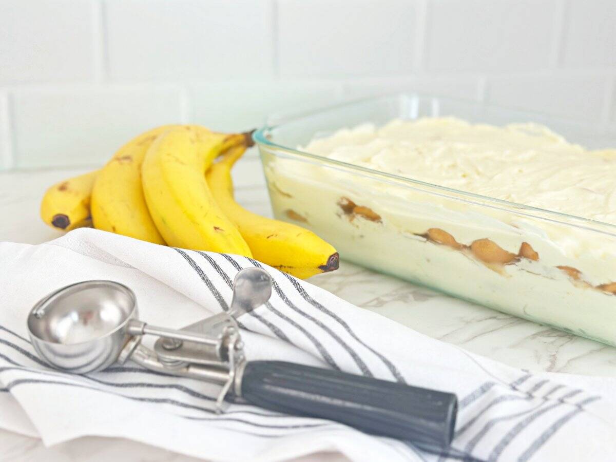 Side view of scoopable banan pudding. Next to a silver ice cream scoop and fresh bananas.