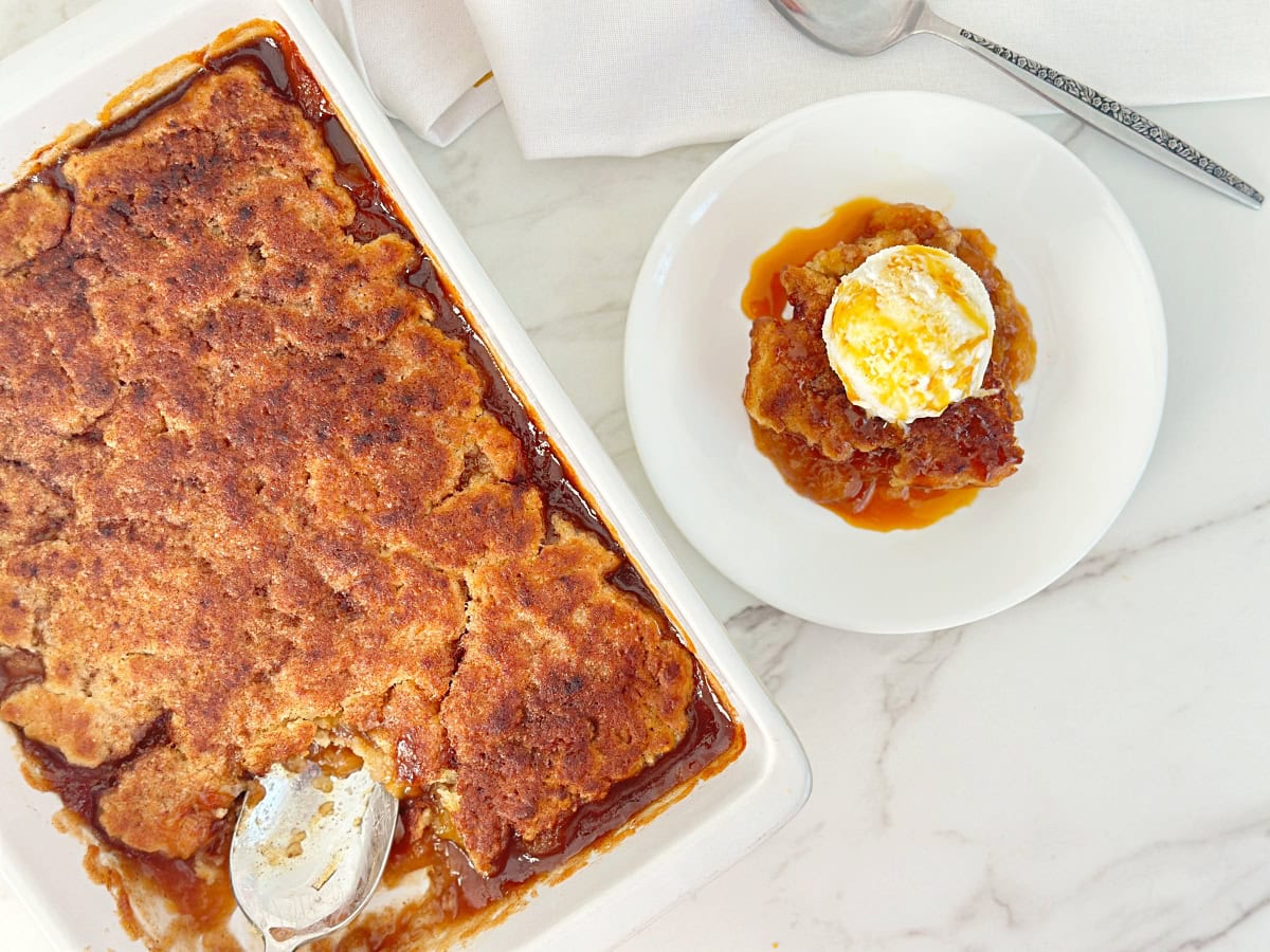 Down view of old fashioned peach cobbler in baking dish. Next to a white plate with peach cobbler with vanilla ice cream.