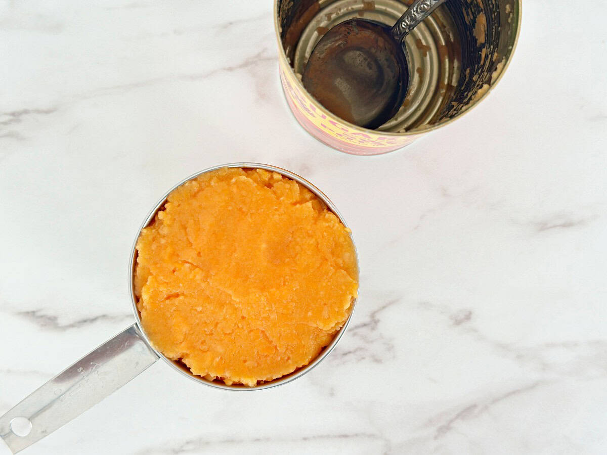 Down view of a silver measuring cup with mashed sweet potato.