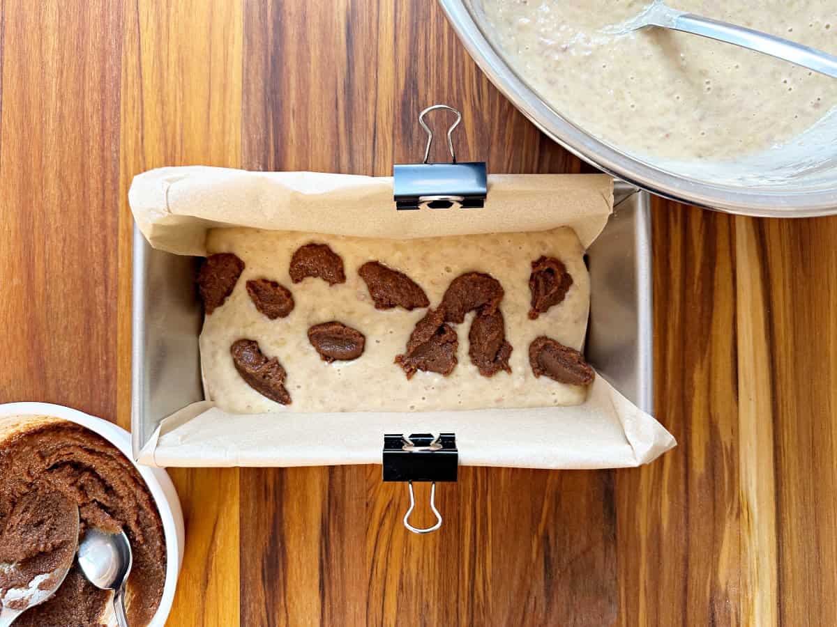 Down view of loaf pan with banana bread mixture and drops of cinnamon swirl mixture.