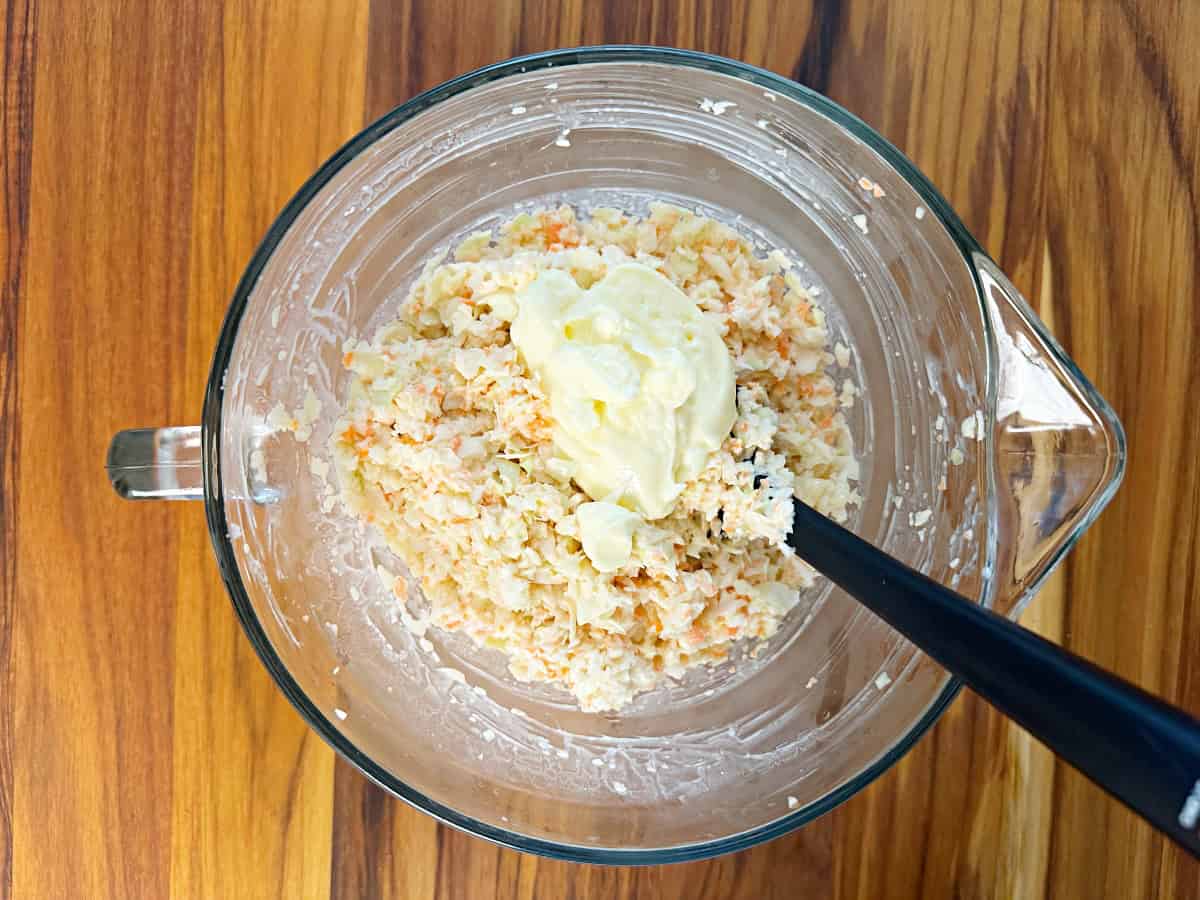 Down view of a glass bowl with coleslaw mixture, mayo, seasoning, and vinegar.