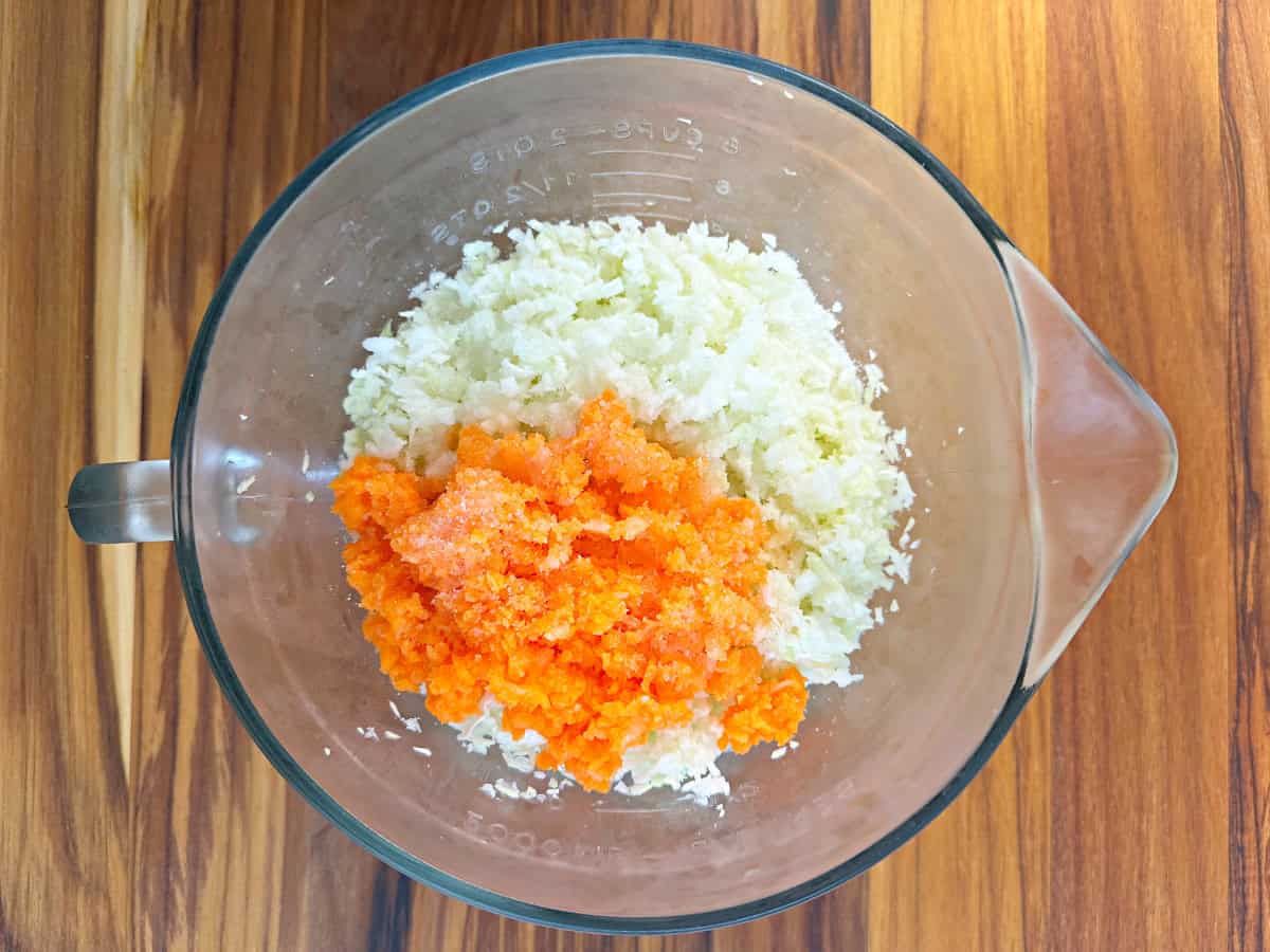 Down view of a glass bowl with chopped cabbage, carrots,and finely shredded onion.
