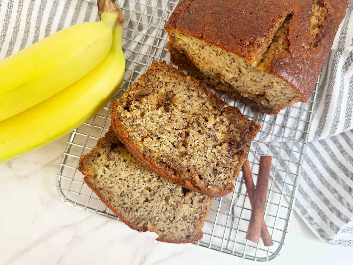 Cinnamon banana bread with oil on silver cooling rack. Slices and a whole loaf.
