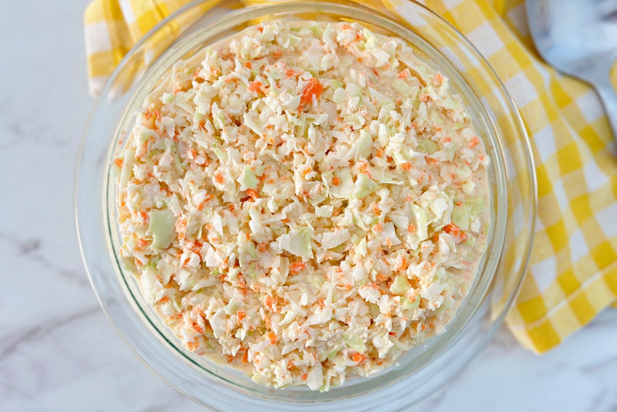 A bowl of southern coleslaw with mayonnaise next to a spoon.