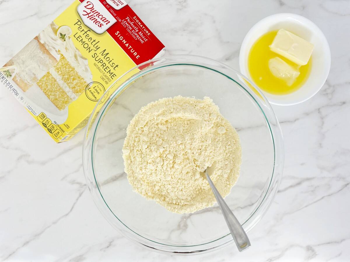 Down view of glass bowl with lemon cake mix, next to a bowl of softened butter.