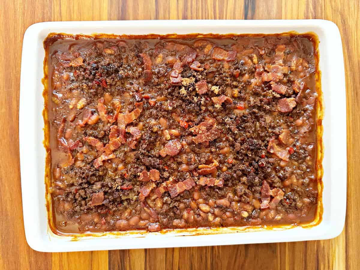 Down view of oven baked cowboy baked beans in white baking dish.