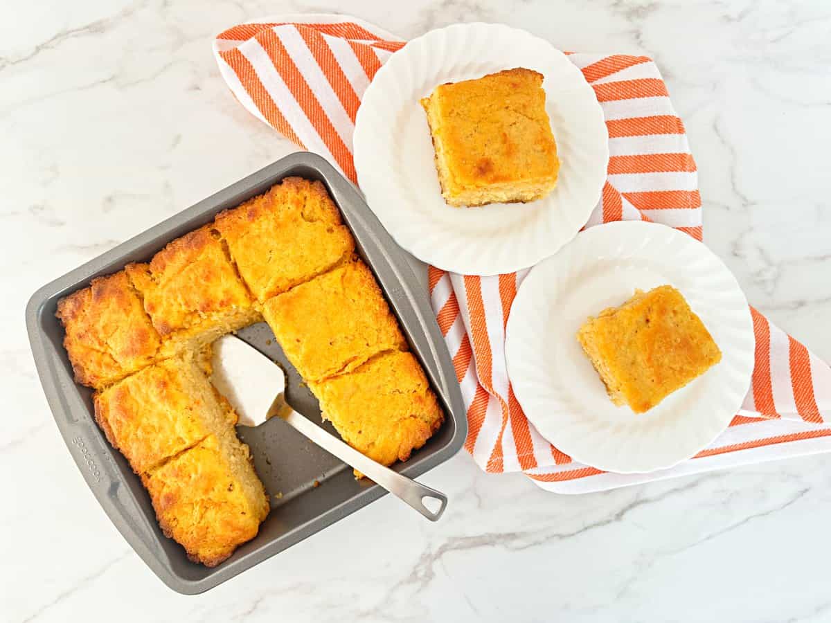 Sweet potato butter swim biscuits baked in a metal baking dish with two pieces on white plates, top view.
