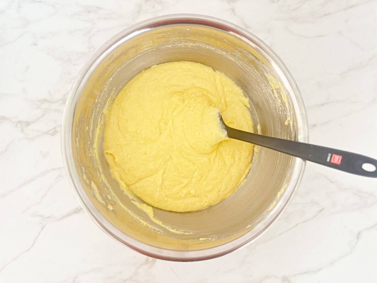 Mixed buttermilk cornbread batter in silver mixing bowl with a rubber spatula, down view.