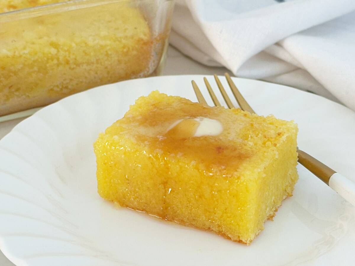 A piece of Jiffy buttermilk cornbread topped with butter and honey on a white plate. Close-up side view.