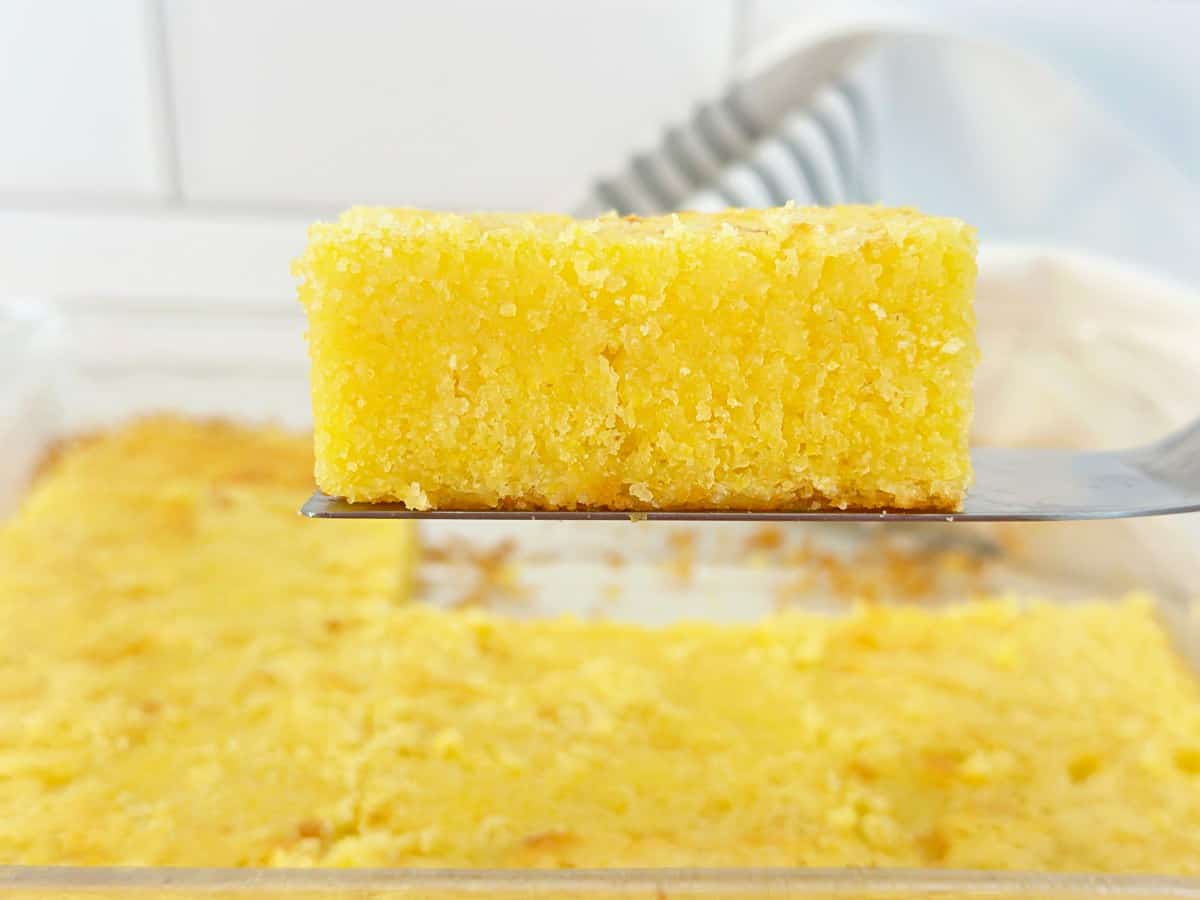 A slice of Jiffy buttermilk cornbread on a silver spatula. Close-up side view to show moist texture.
