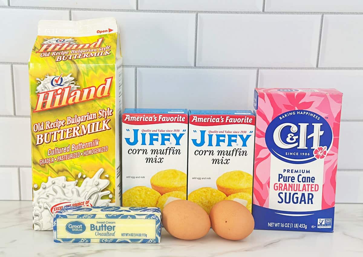 Carton of buttermilk, two boxes of Jiffy corn muffin mix, box of granulated sugar, stick of butter, and two eggs.