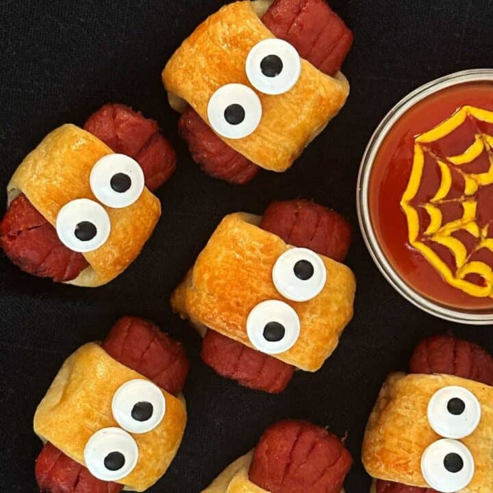 Spider dogs with crescent dough and candy eyes for Halloween on a black plate.