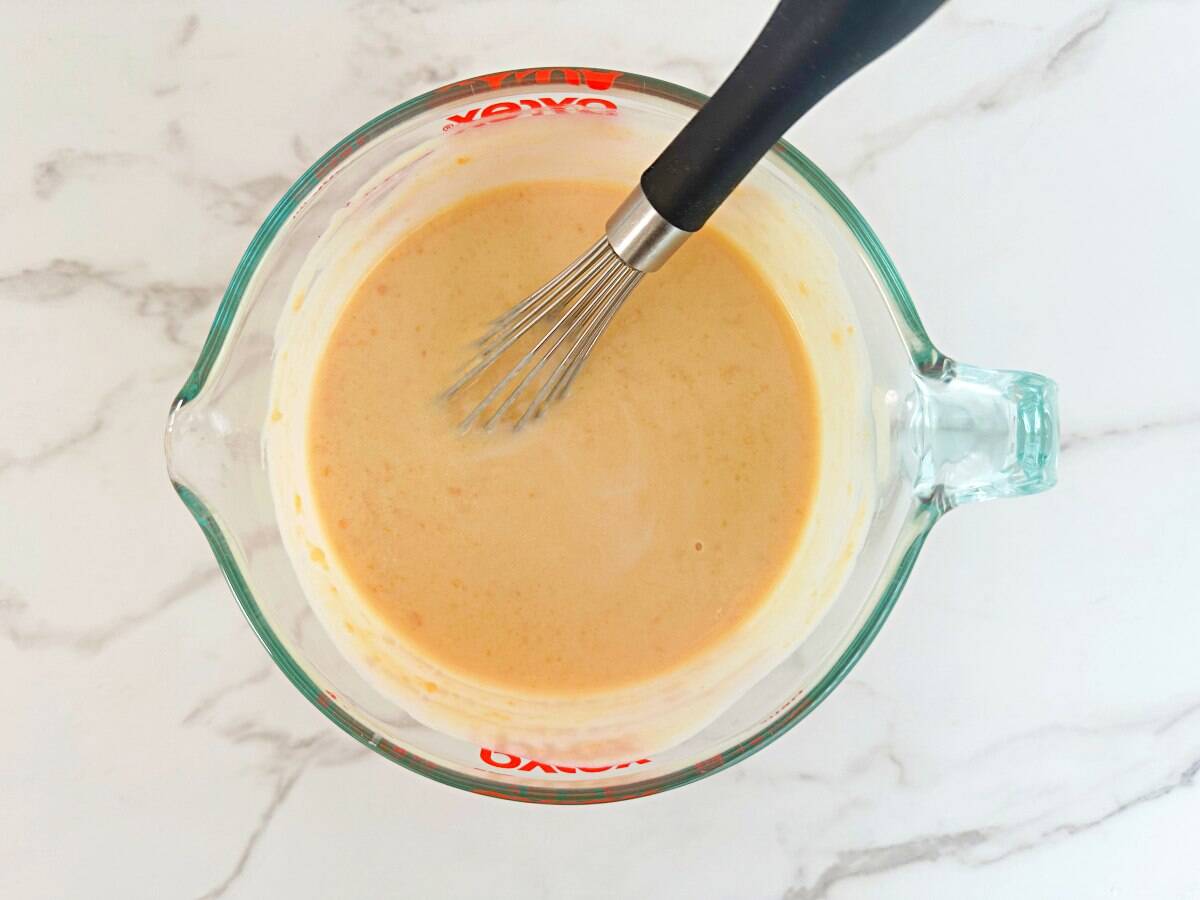 Large glass measuring cup with mixed wet ingredients and a whisk.