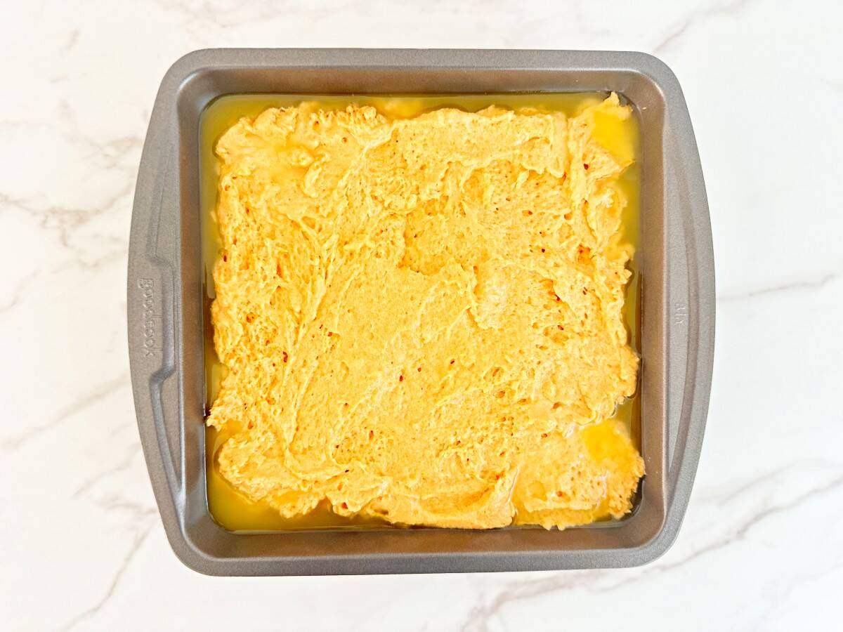 A metal baking dish with melted butter and biscuit dough in a single layer.