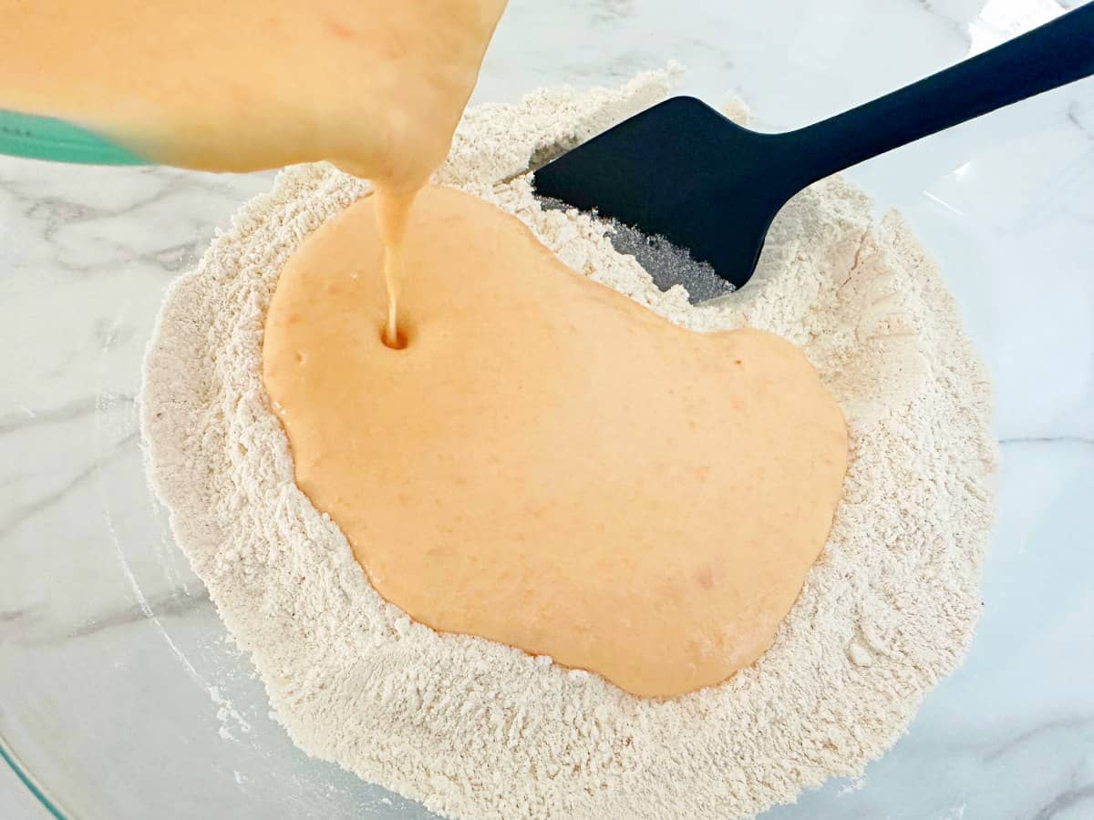 Measuring cup pouring wet ingredients into a mixing bowl with dry ingredients.