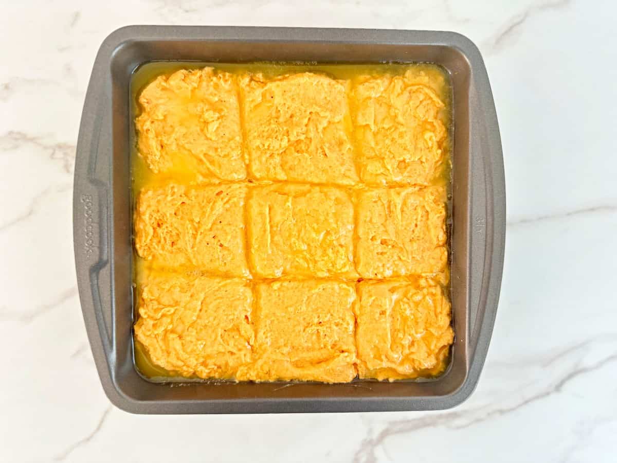 A metal baking dish with melted butter and cut biscuit dough.