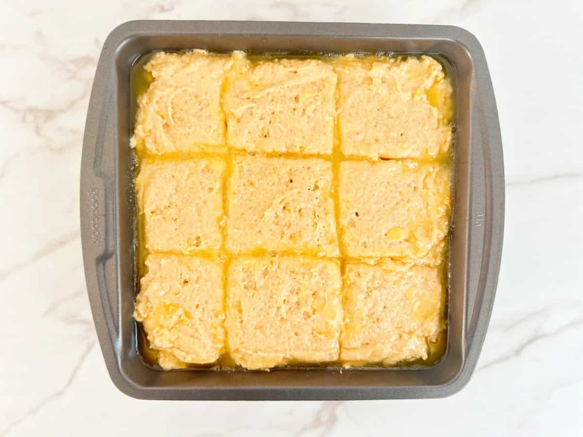 A metal baking dish with melted butter and cut biscuit dough.