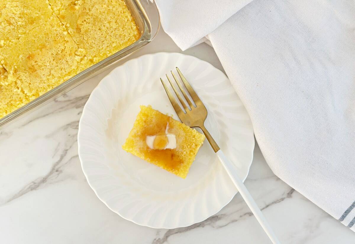 A piece of Jiffy buttermilk cornbread topped with butter and honey on a white plate, down view.