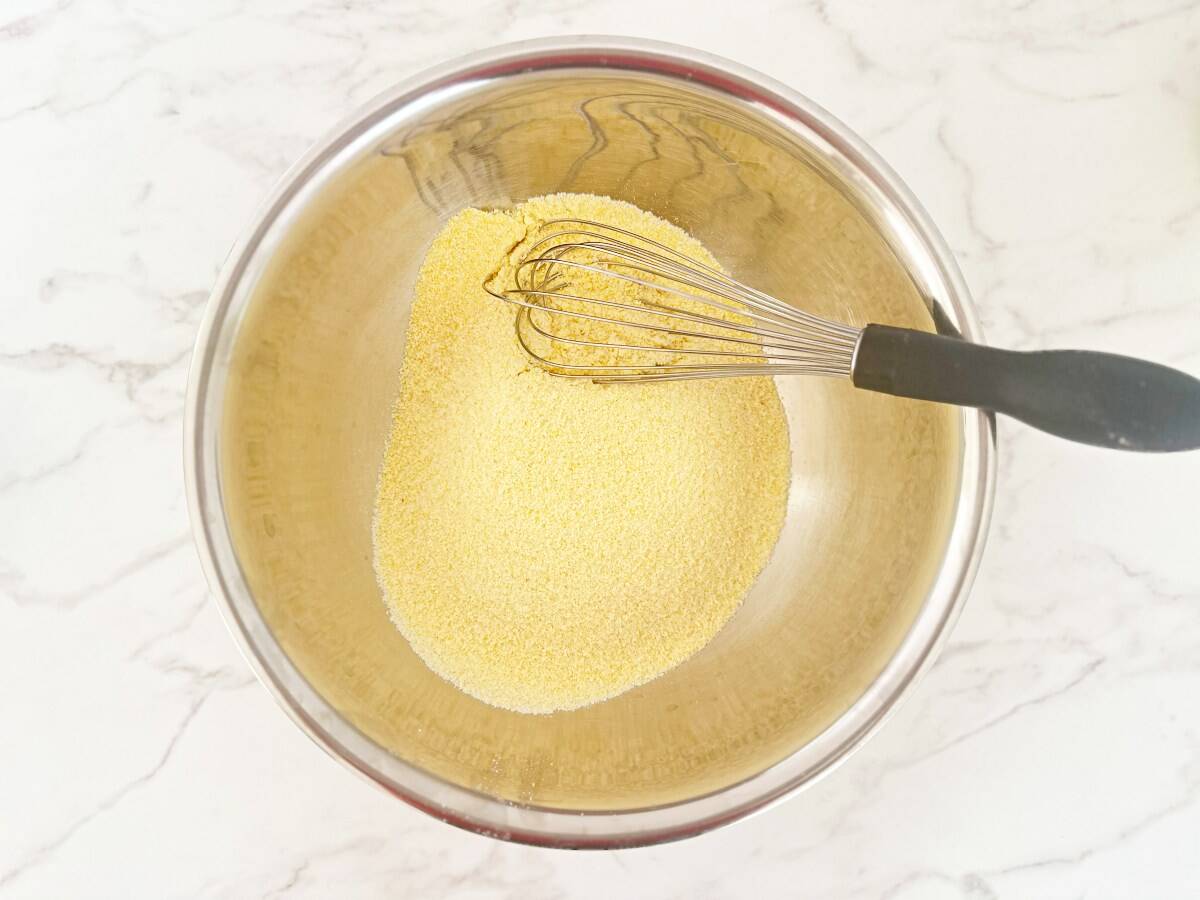 Sifted jiffy muffin mix in a silver mixing bowl with a whisk, down view.