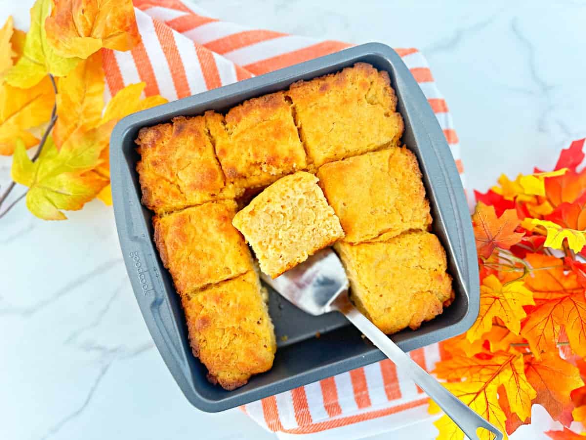 Sweet potato butter swim biscuits in a metal baking dish. One biscuit is cut to show moist texture. Next to a silver spatual and decorative fall leaves.